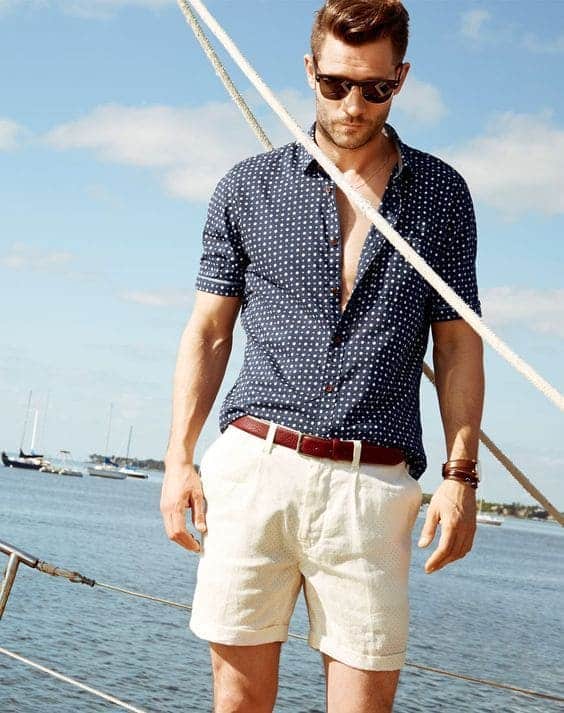 a man wearing a white and blue casual outfit standing on a boat