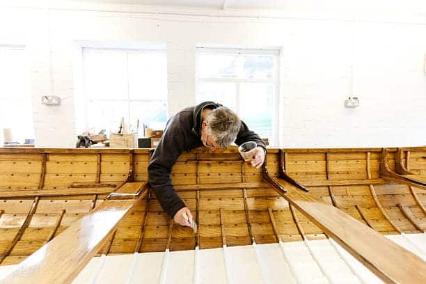 A boat builder paints varnish onto the interior of a traditional, hand built wooden gig boat