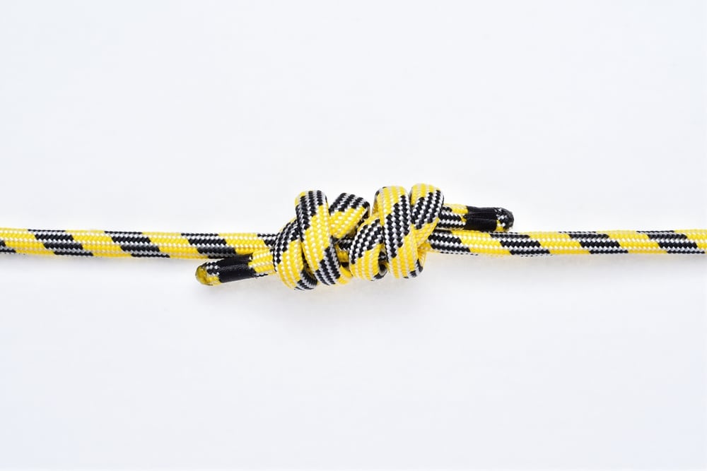 Double Fisherman's knot on yellow and black nylon rope on white background.