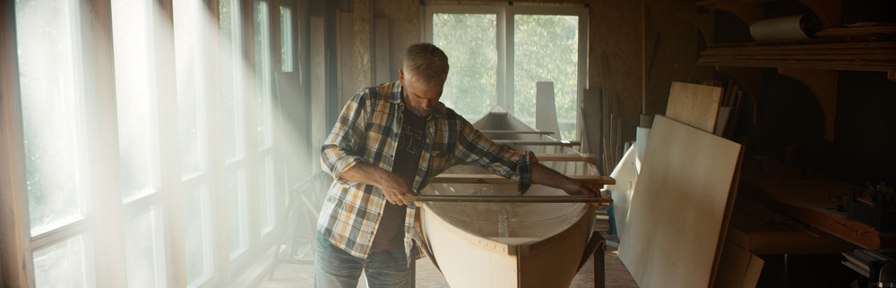 Caucasian Male Using Measure Tape While Building A Canoe In