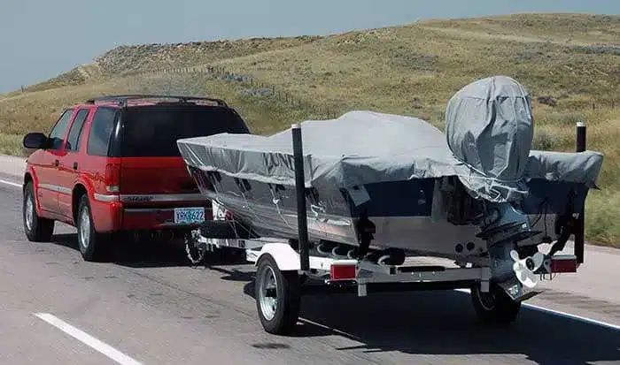 A view of a boat with a cover on being trailered behind a red car