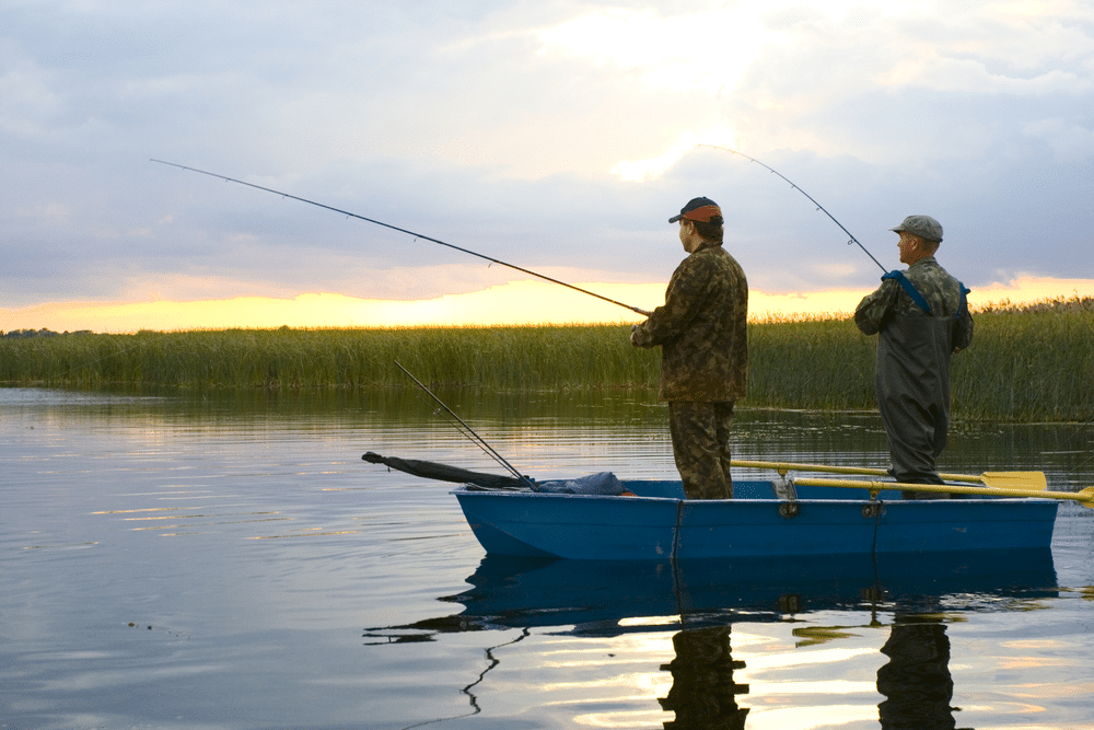 A view of two people fishing with a rod standing on a boat in a lake